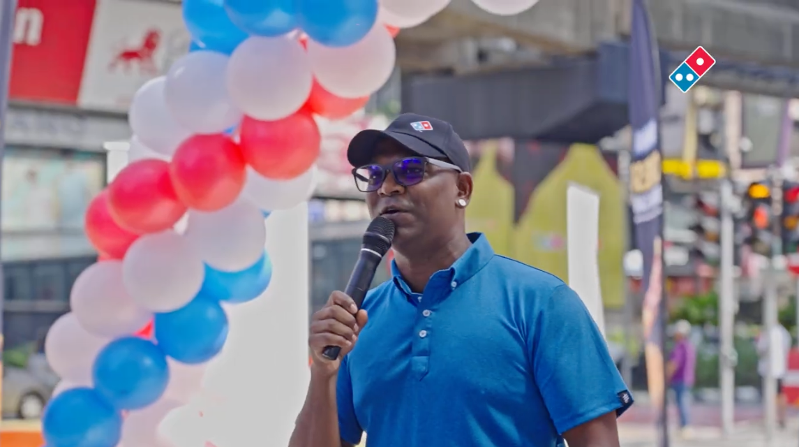 Event host speaking into a microphone beside a balloon arch