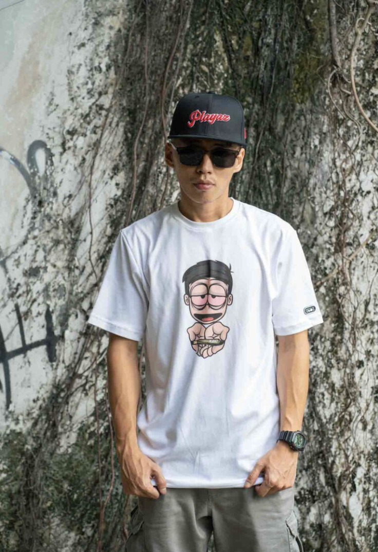 Model in white Playaz cartoon tee against a vine wall